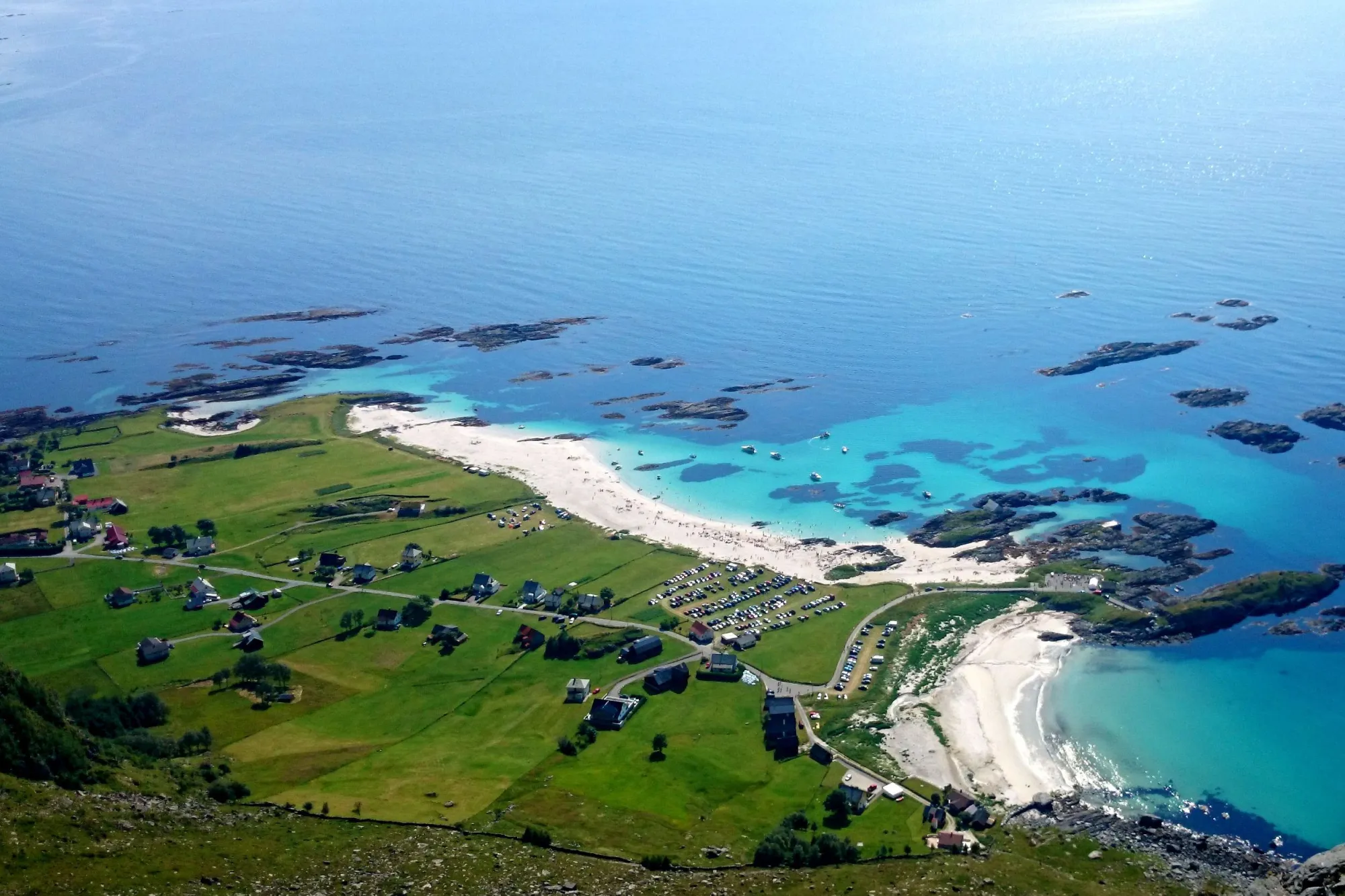Grotlesanden, Luftfoto av kystlandskap med grønne jorder, hus og veg, kvit sandstrand og turkis sjø med små øyar..