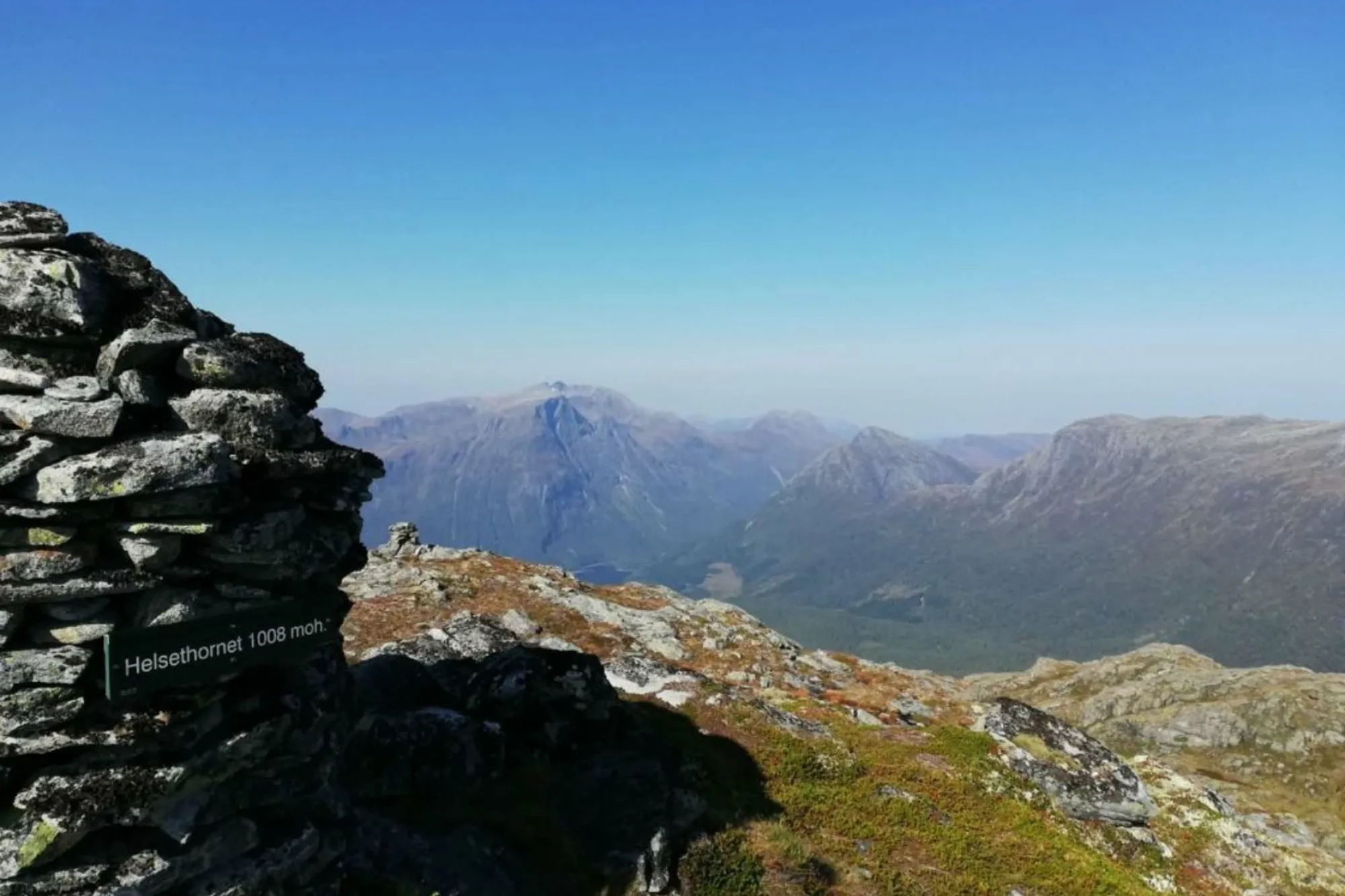 Steinvarde på Helsethornet, utsikt over fjell og dalar under klar blå himmel..