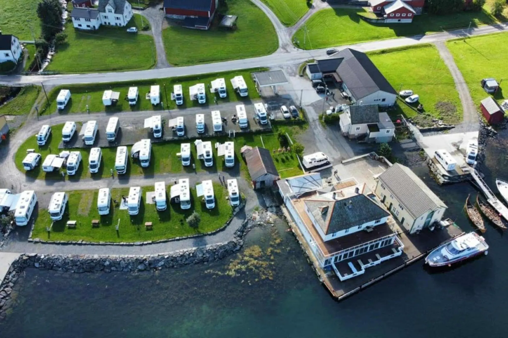 Luftfoto av Davik Fjordparadis i Bremanger -bubilpark på grøne plenar ved sjøen, med bygningar, kai og båtar i ei lita hamn..