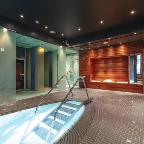 Innandørs spa med opplyst bassengtrapp, flislagt golv, glasveggar og ein varm trevegg med sitjeplass..